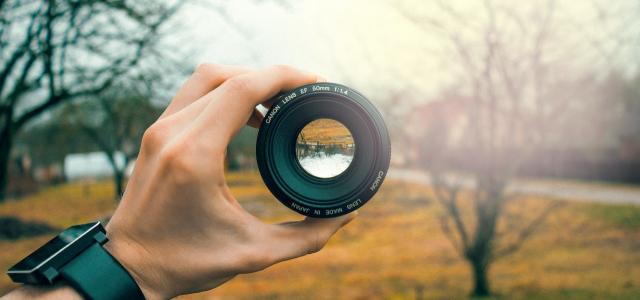 Person holding a camera lens in a field. The view of the field within the camera lens is upside down.